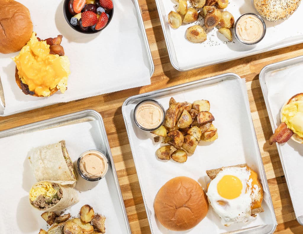 Breakfast catering spread — egg sandwiches, a breakfast burrito and roasted potatoes on a shared table
